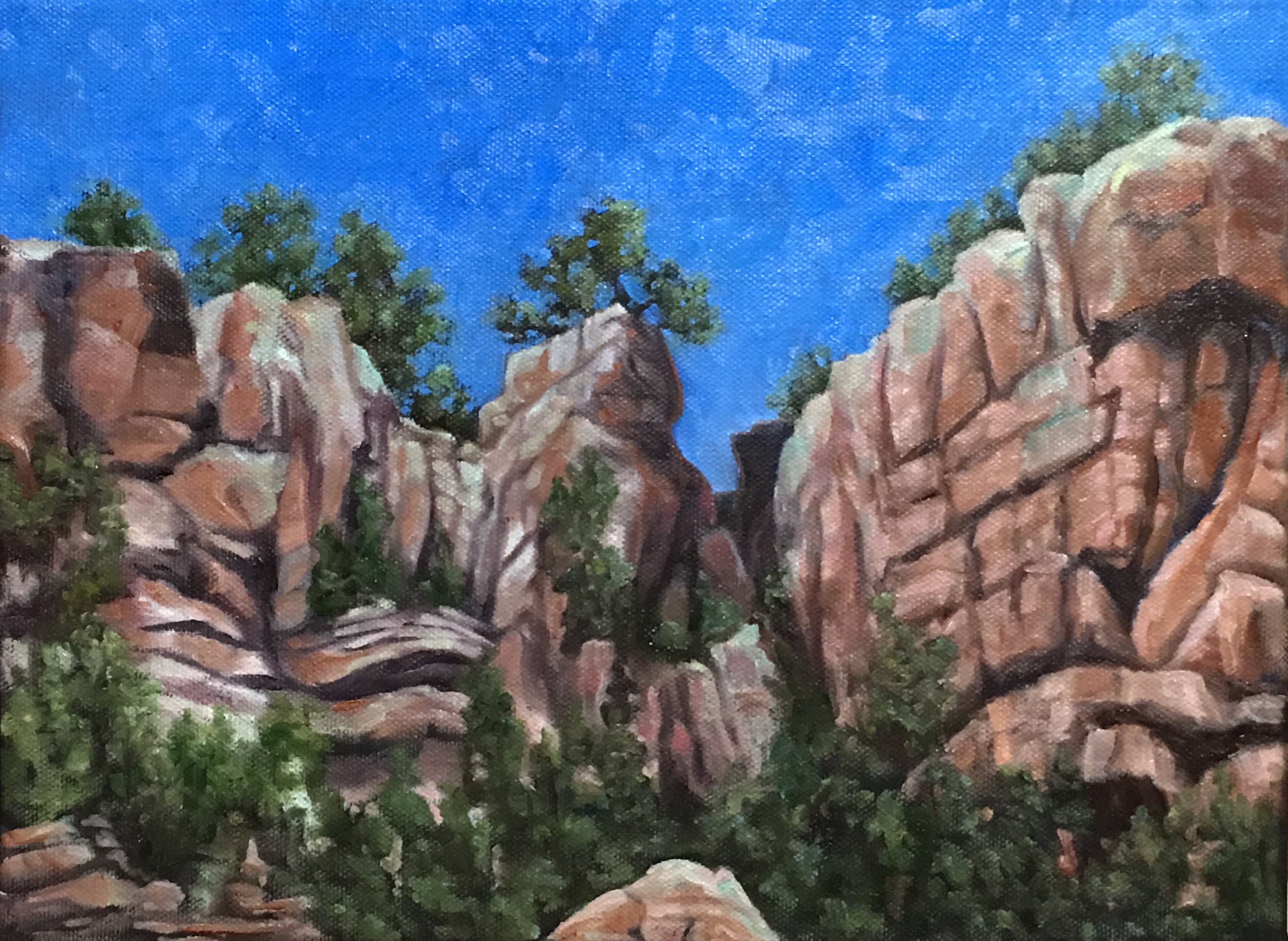 Red rock formations with green trees under bright blue sky